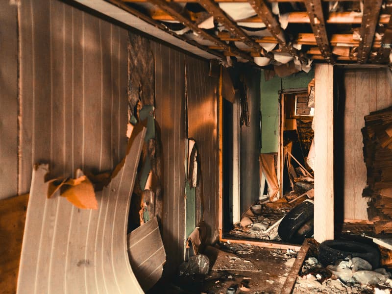 Burned interior of a residential hallway showing collapsed ceiling panels and structural damage, emphasizing the real-world importance of Homeowners Insurance coverage after a fire.

