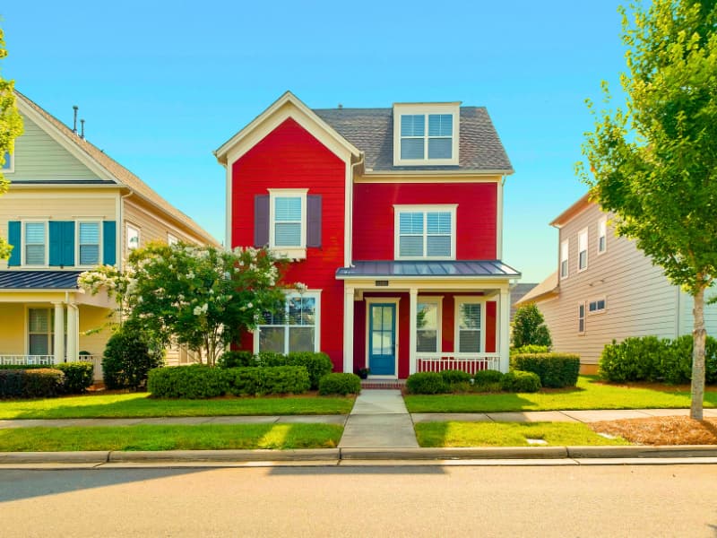 A brightly colored red suburban home under a clear blue sky, representing the kind of property evaluated when comparing Homeowners Insurance Quotes online in 2025.