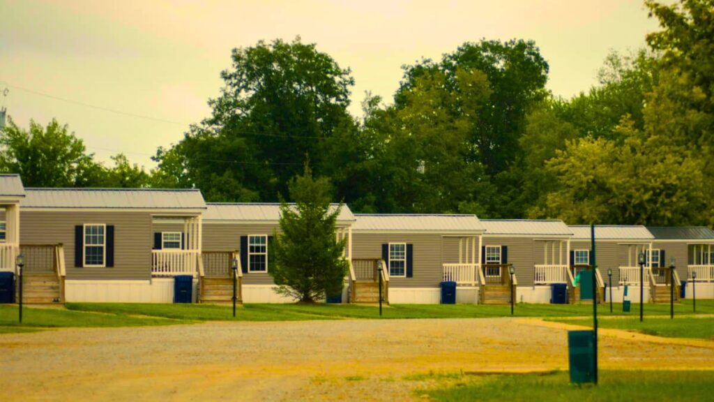 Row of modern mobile homes in a quiet neighborhood with trees in the background under a cloudy sky.
