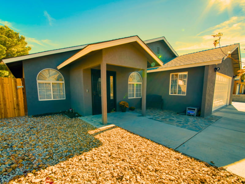 Single-story suburban home with arched windows and xeriscape front yard under a bright blue sky.