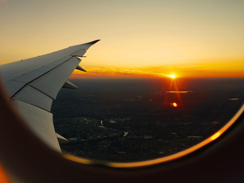 Sunset view through an airplane window as the flight approaches a distant city—symbolizing how quickly a dream trip can shift into crisis mode without proper travel insurance for international travel in place.