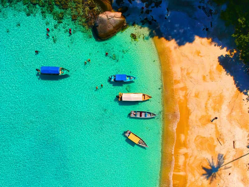 Tropical beach with vibrant boats floating in crystal-clear water—looks like the perfect escape, but one accident or sudden illness here shows why travel insurance for international travel matters more than sunscreen.
