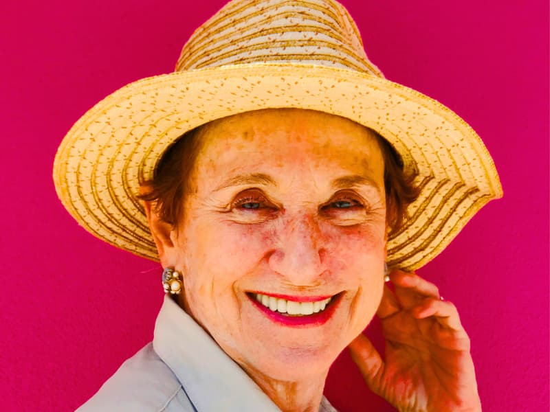 Smiling retired woman aged 60+ standing against a pink background, representing a homeowner demographic that often qualifies for senior-specific Homeowners Insurance Discounts due to lower claim risk and lifestyle.