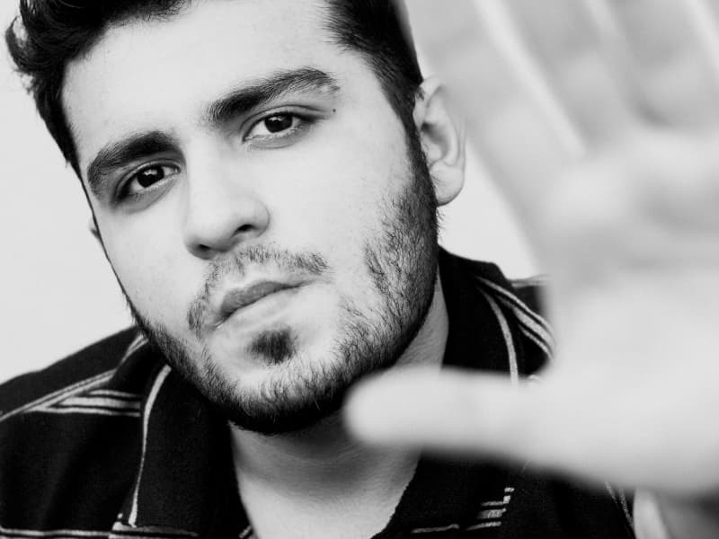 A thoughtful young man raising his hand in a calm “not so fast” gesture, representing a homeowner who knows how to spot bad deals and avoid the most common traps when chasing Homeowners Insurance Discounts.