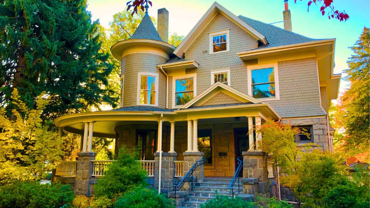 Historic Victorian-style home with wrap-around porch surrounded by trees in a quiet zip code area – relevant for House Insurance Near Me location-based risk assessment.