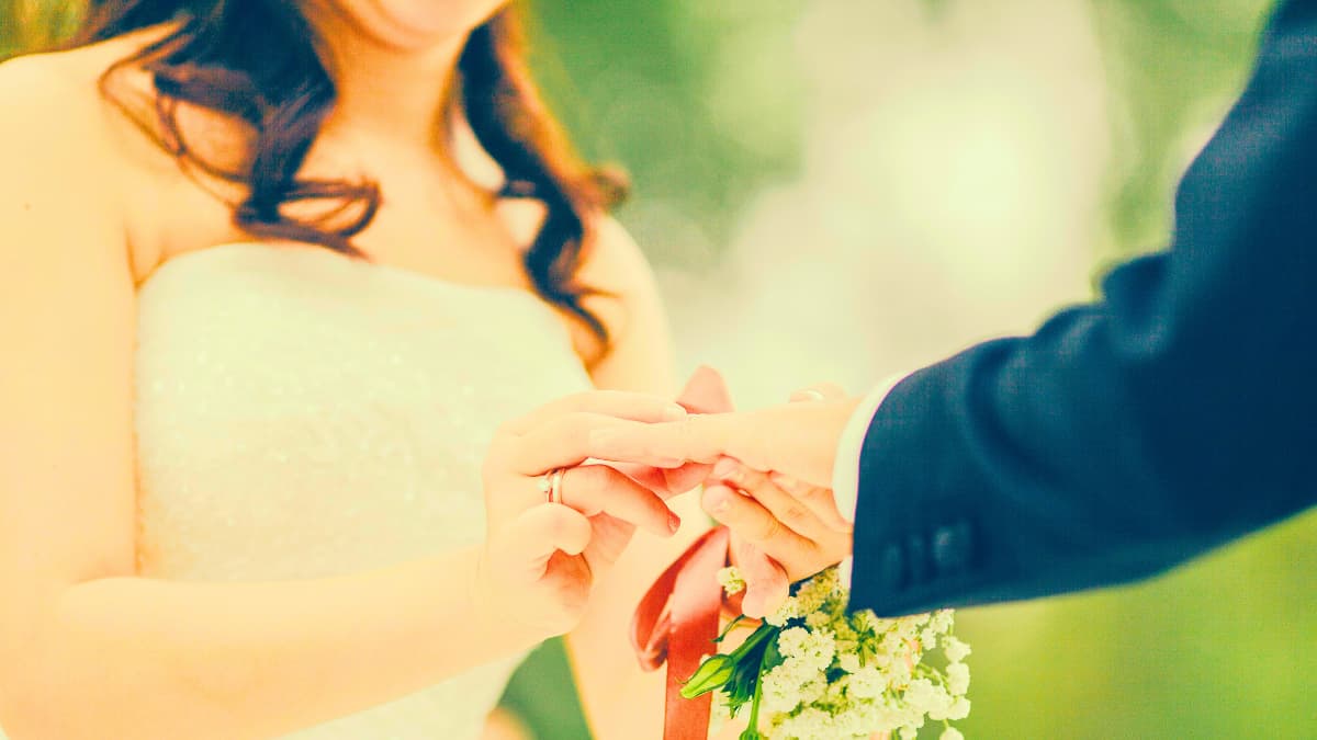 Bride placing a ring on the groom’s finger, close-up of hands with a white bouquet and soft bokeh—remember to secure wedding venue insurance.