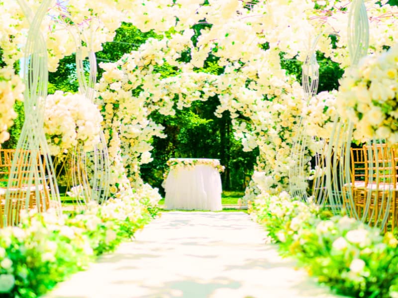 Sunlit outdoor aisle framed by white flower arches and chairs—detailed décor that often requires wedding venue insurance.